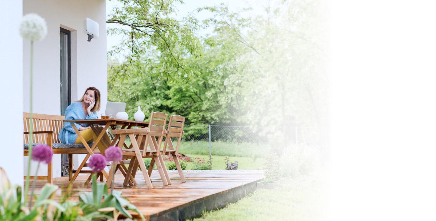 Woman sitting outside of her home at a wood table talking on the phone over fixed wireless